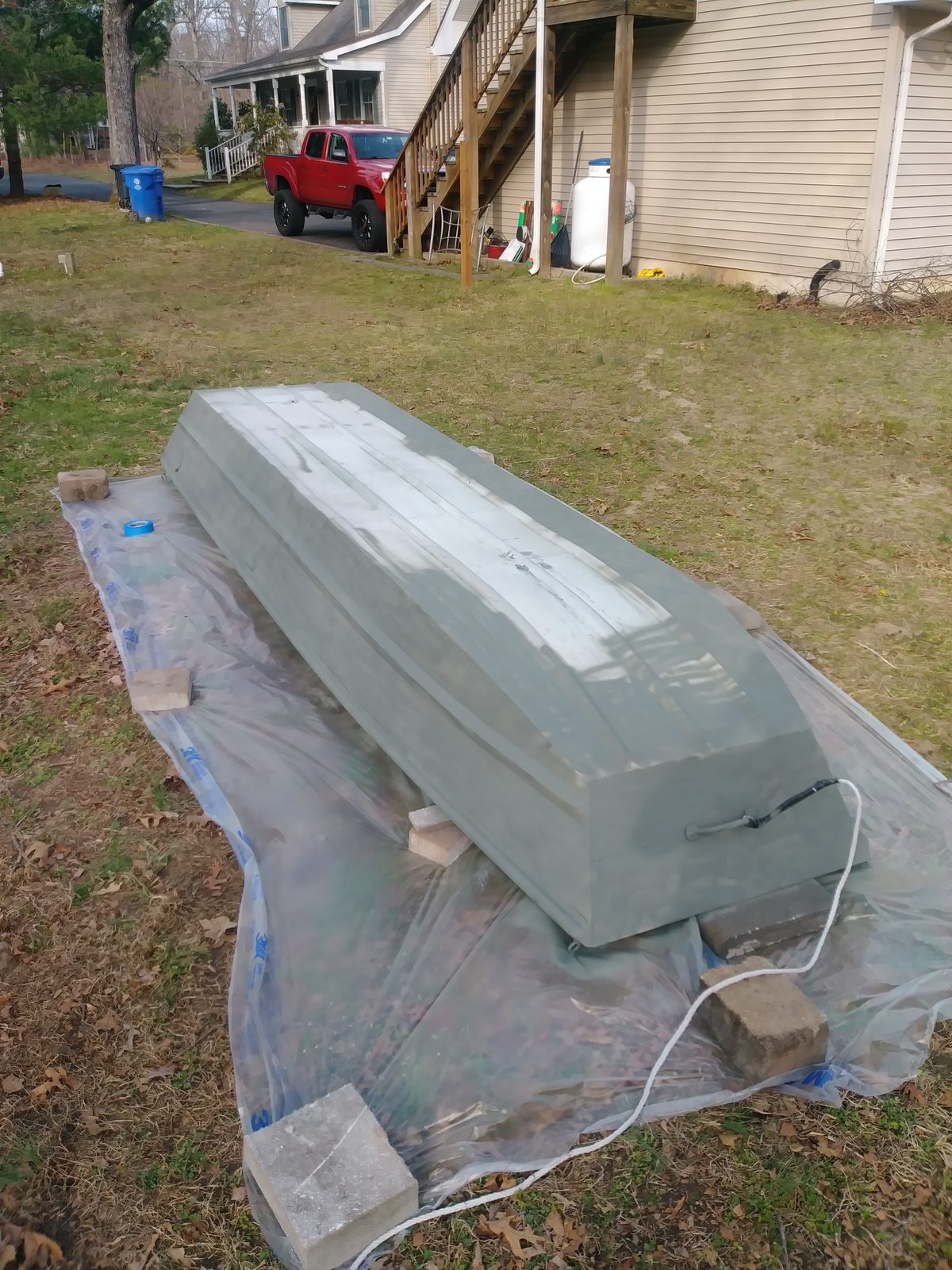 Hull tarped on blocks with primer coat drying, house and truck in the background